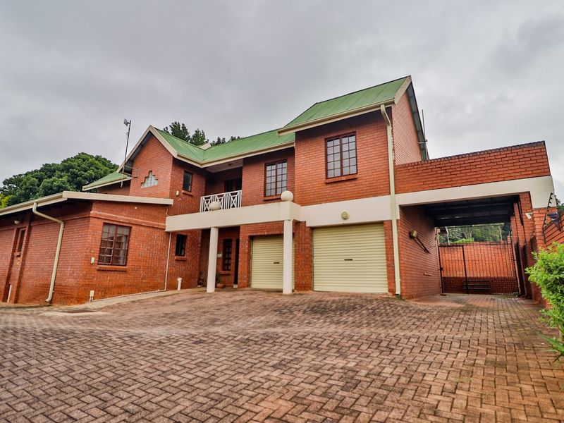 A well-maintained double-story face brick house featuring a green metal roof, double garage, paved driveway, and an upper-level balcony.