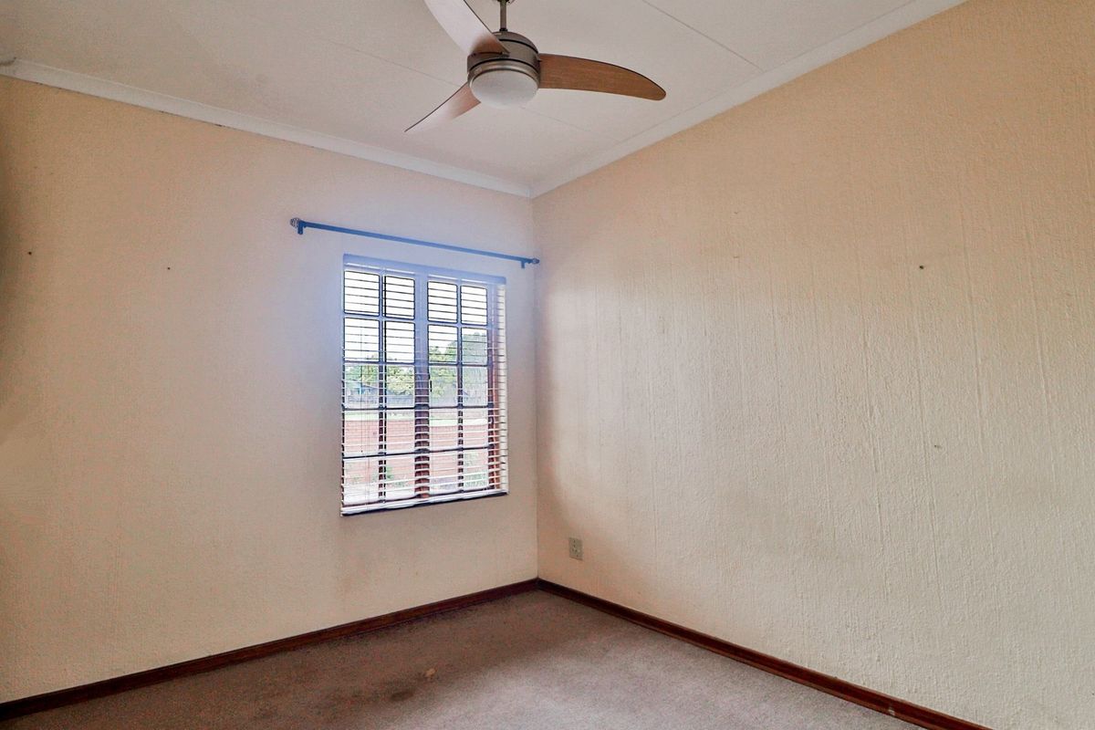 An empty bedroom featuring a ceiling fan, carpeted flooring, and a window with fitted blinds, offering a blank canvas for personalization.