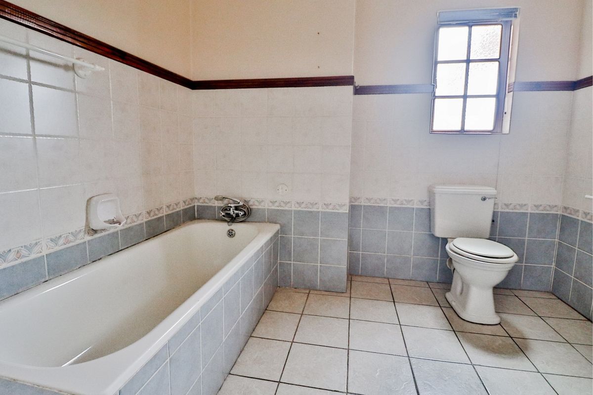 A dated bathroom featuring a built-in bathtub, toilet, and tiled finishes, offering a blank canvas for a modern renovation.