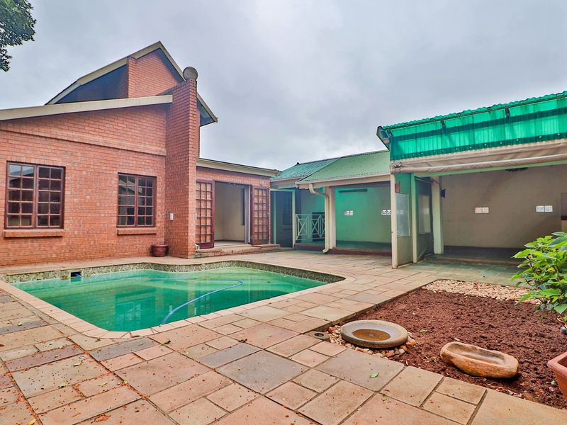 Rear courtyard featuring a swimming pool, paved patio area, and covered outdoor space with brick and corrugated roof construction.