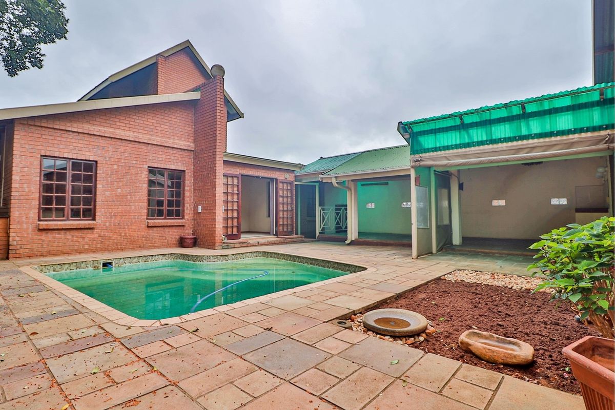 Rear courtyard featuring a swimming pool, paved patio area, and covered outdoor space with brick and corrugated roof construction.