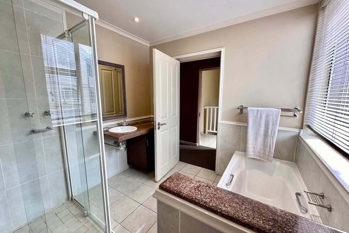 A functional bathroom featuring a glass-enclosed shower, a built-in bathtub with stone-look surround, and a vanity unit.