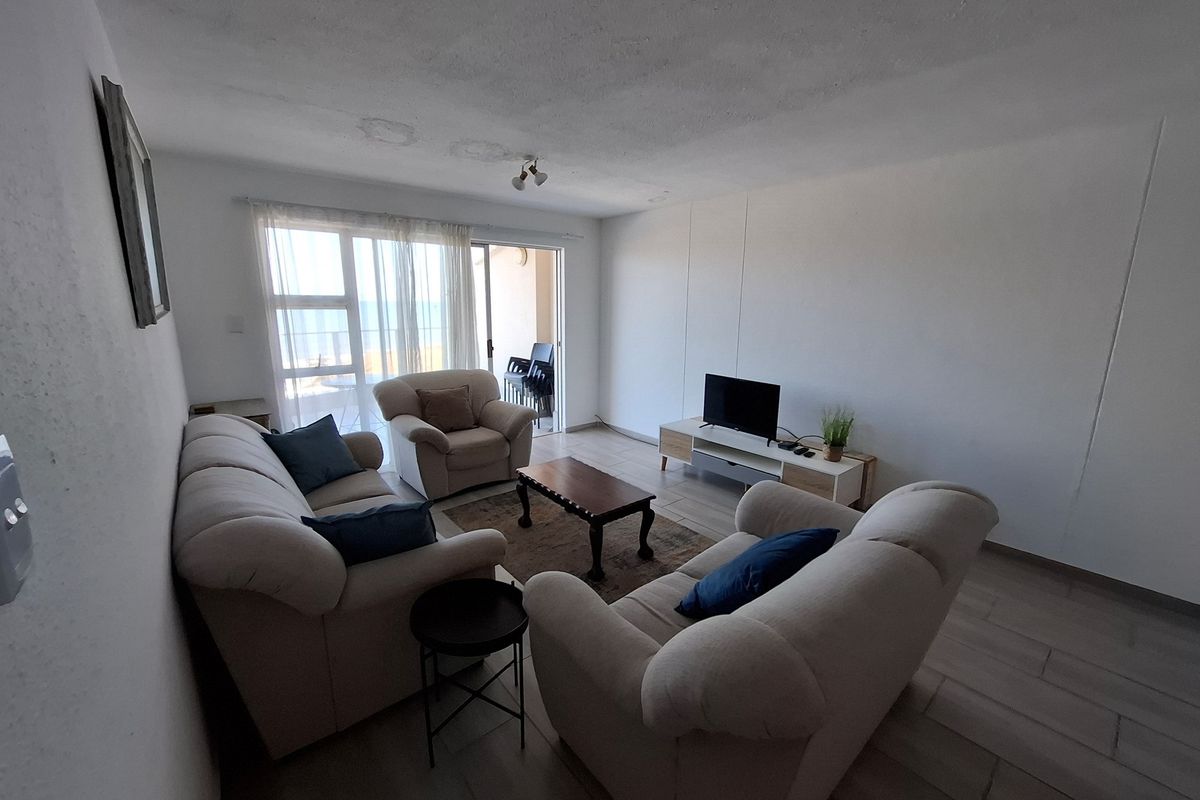 A living room featuring tiled flooring and sliding glass doors leading to a balcony, with visible ceiling damage requiring repair.