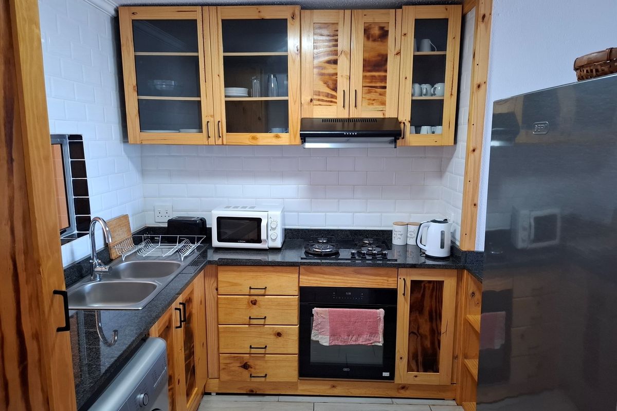 Compact kitchen featuring natural wood cabinetry, granite countertops, subway tile backsplash, built-in oven, gas hob, and stainless steel double sink.