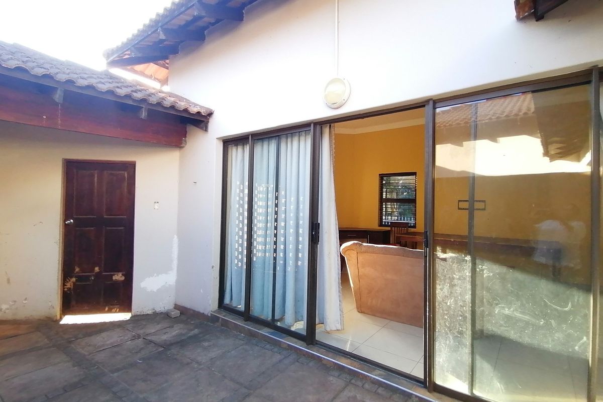 Rear exterior view showing a paved patio area, sliding glass doors leading into the living space, and a side timber door.
