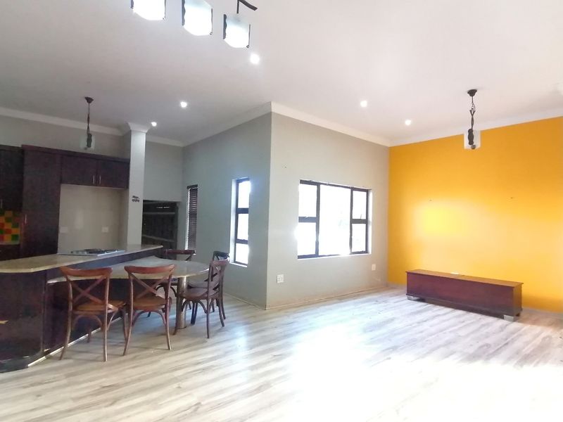 Spacious open-plan living and kitchen area featuring modern laminate flooring, built-in cabinetry with a breakfast island, and contemporary lighting fixtures.