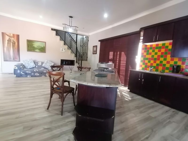 Open plan living and kitchen area featuring a central island, dark cabinetry, laminate flooring, and a staircase with a decorative wrought iron balustrade.