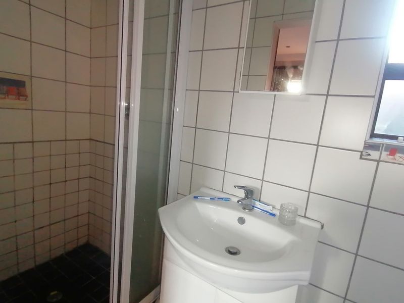 A functional bathroom featuring a shower enclosure, pedestal basin with mixer tap, and tiled wall finishes.