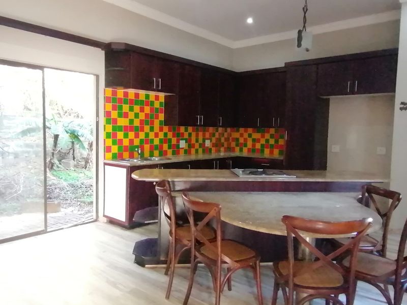 Kitchen featuring dark wood cabinetry, stone countertops, a built-in hob, and a vibrant multi-colored tile backsplash with direct access to the garden.