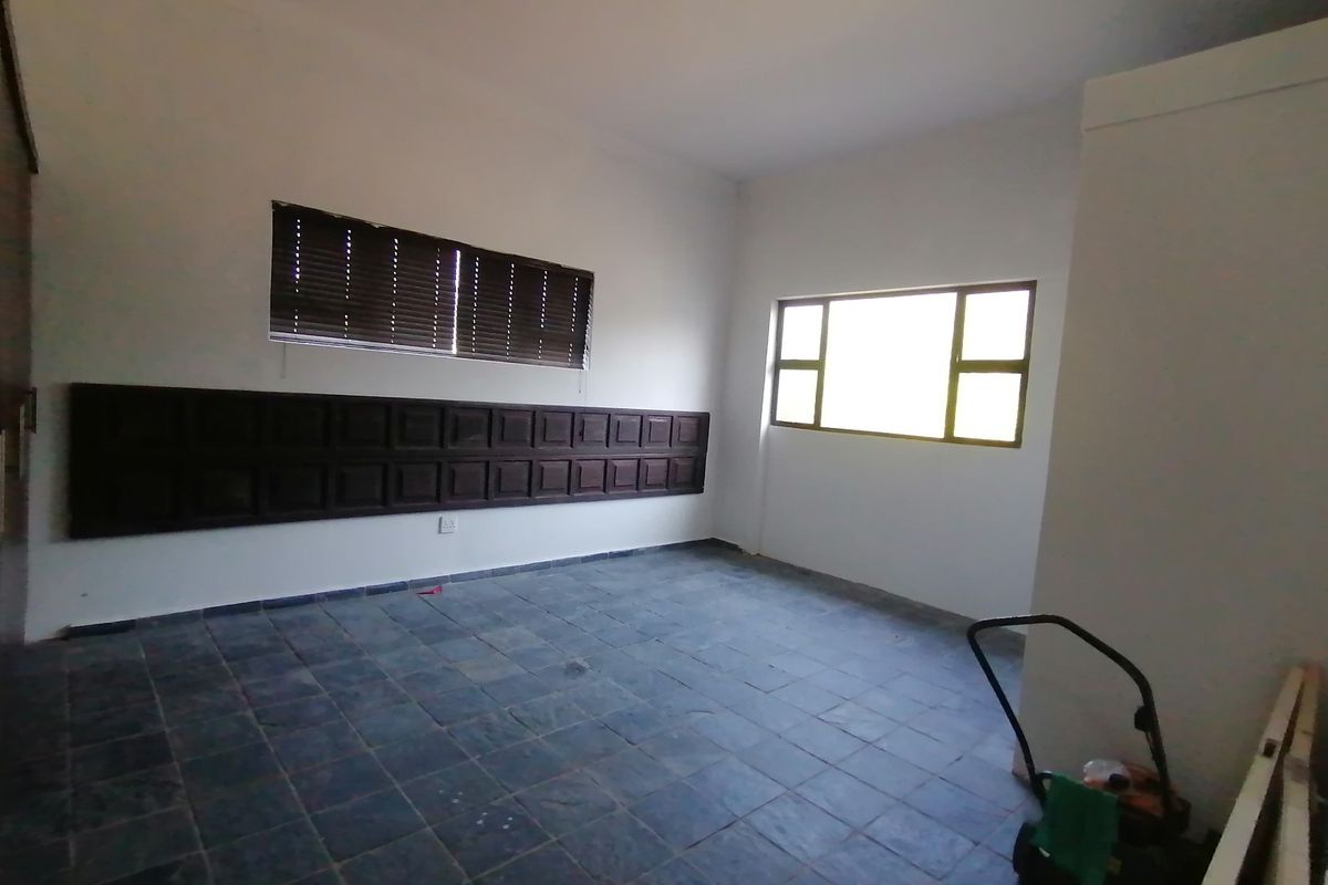 An empty bedroom featuring slate tile flooring, decorative wooden wall paneling, and aluminium-framed windows with fitted venetian blinds.