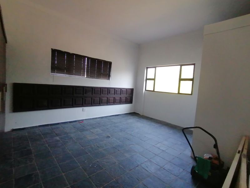 An empty bedroom featuring slate tile flooring, decorative wooden wall paneling, and aluminium-framed windows with fitted venetian blinds.