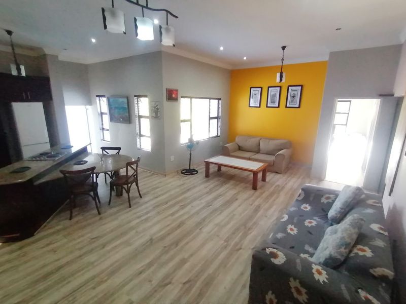 An open-plan living and kitchen area featuring light wood-look laminate flooring, a kitchen island with a hob, and a vibrant yellow accent wall.