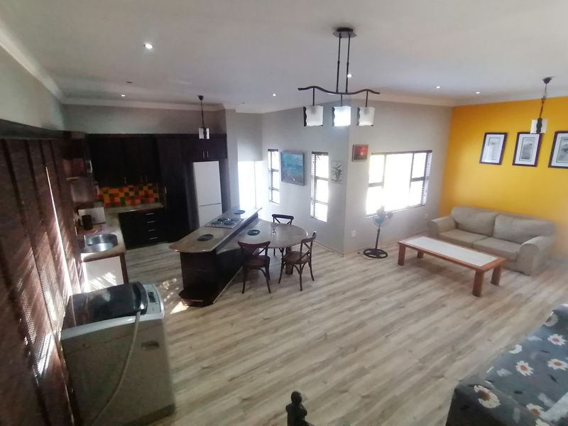 Spacious open-plan living area featuring a modern kitchen with island, laminate flooring, and bright accent wall, creating a functional and inviting home layout.