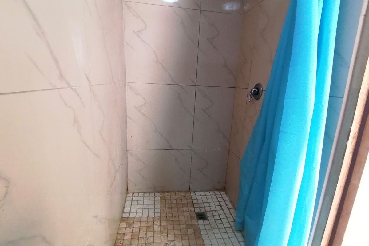A compact shower enclosure featuring marble-effect wall tiles and mosaic floor tiling, currently requiring maintenance and cleaning of the floor surfaces.