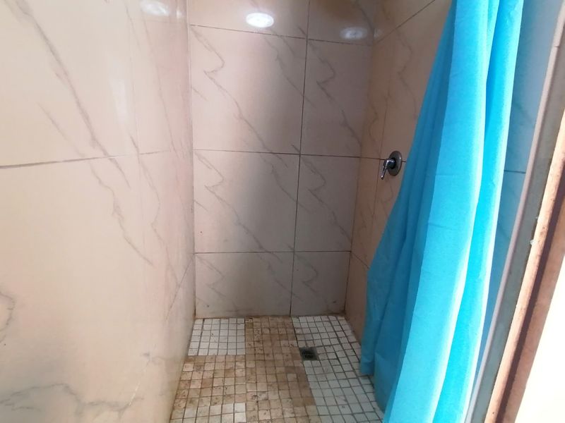 A compact shower enclosure featuring marble-effect wall tiles and mosaic floor tiling, currently requiring maintenance and cleaning of the floor surfaces.
