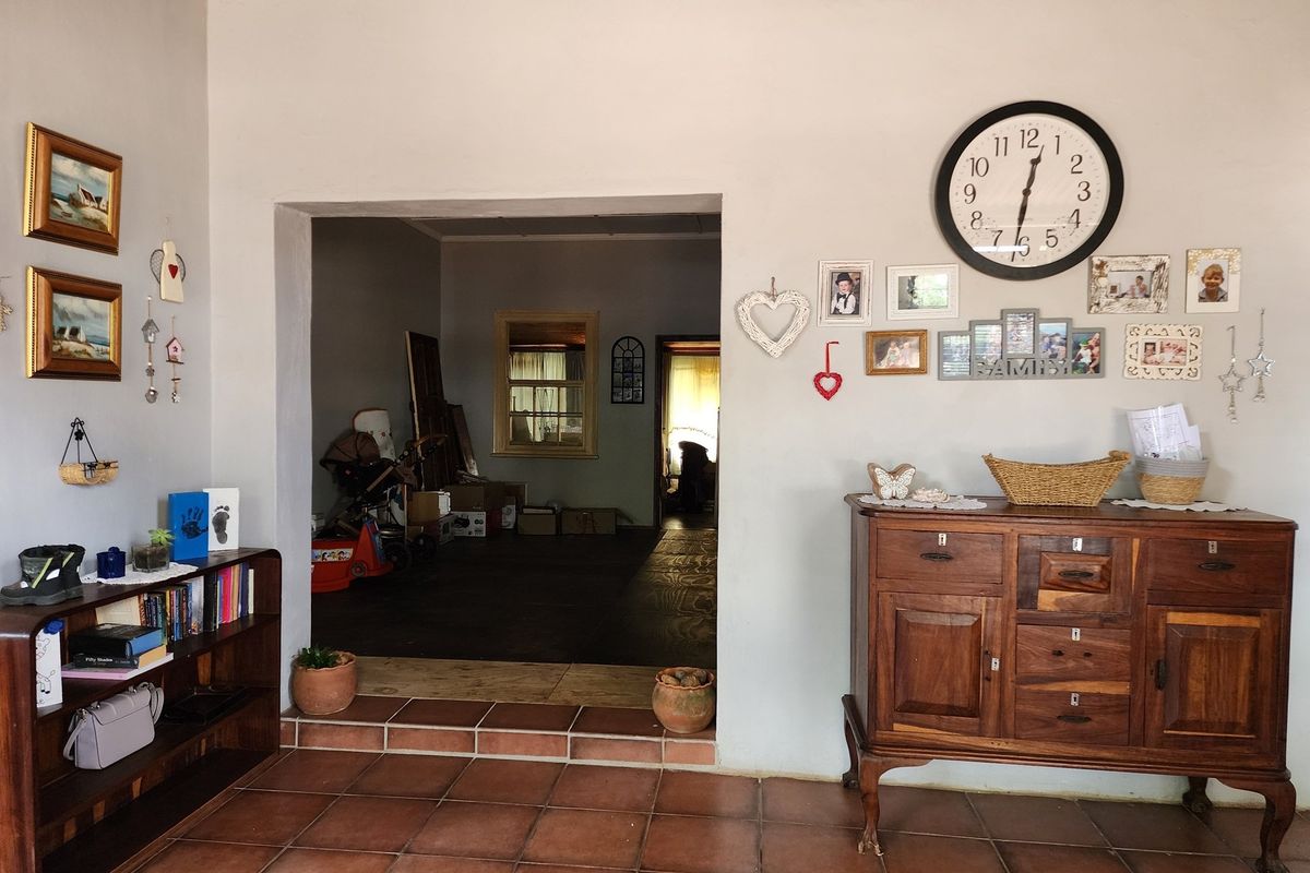 Interior view showing a transition between two living spaces with terracotta floor tiles and a wide doorway opening into an adjacent room.