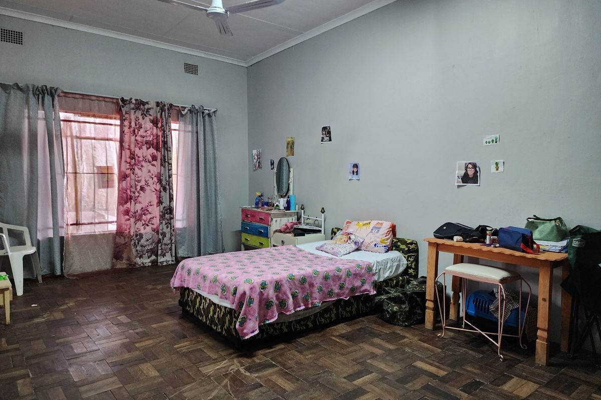 A spacious bedroom featuring traditional parquet wood flooring, large windows with natural light, and a ceiling fan.