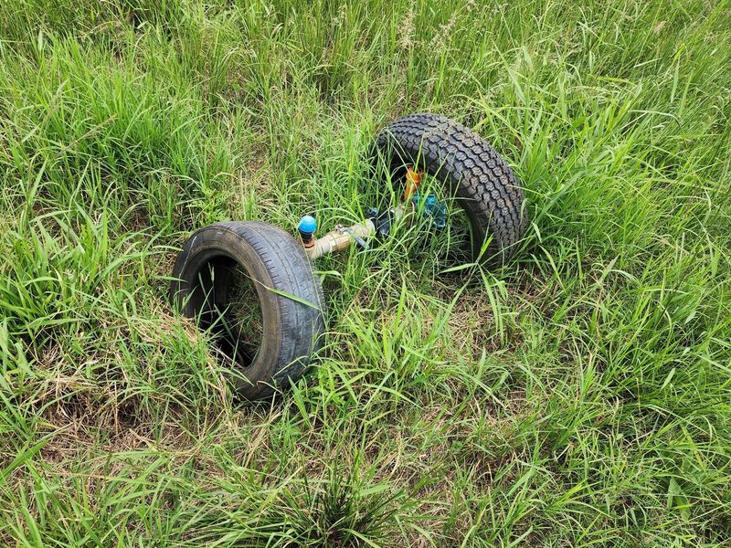An abandoned axle and tire assembly discarded in an overgrown field on the farm property.