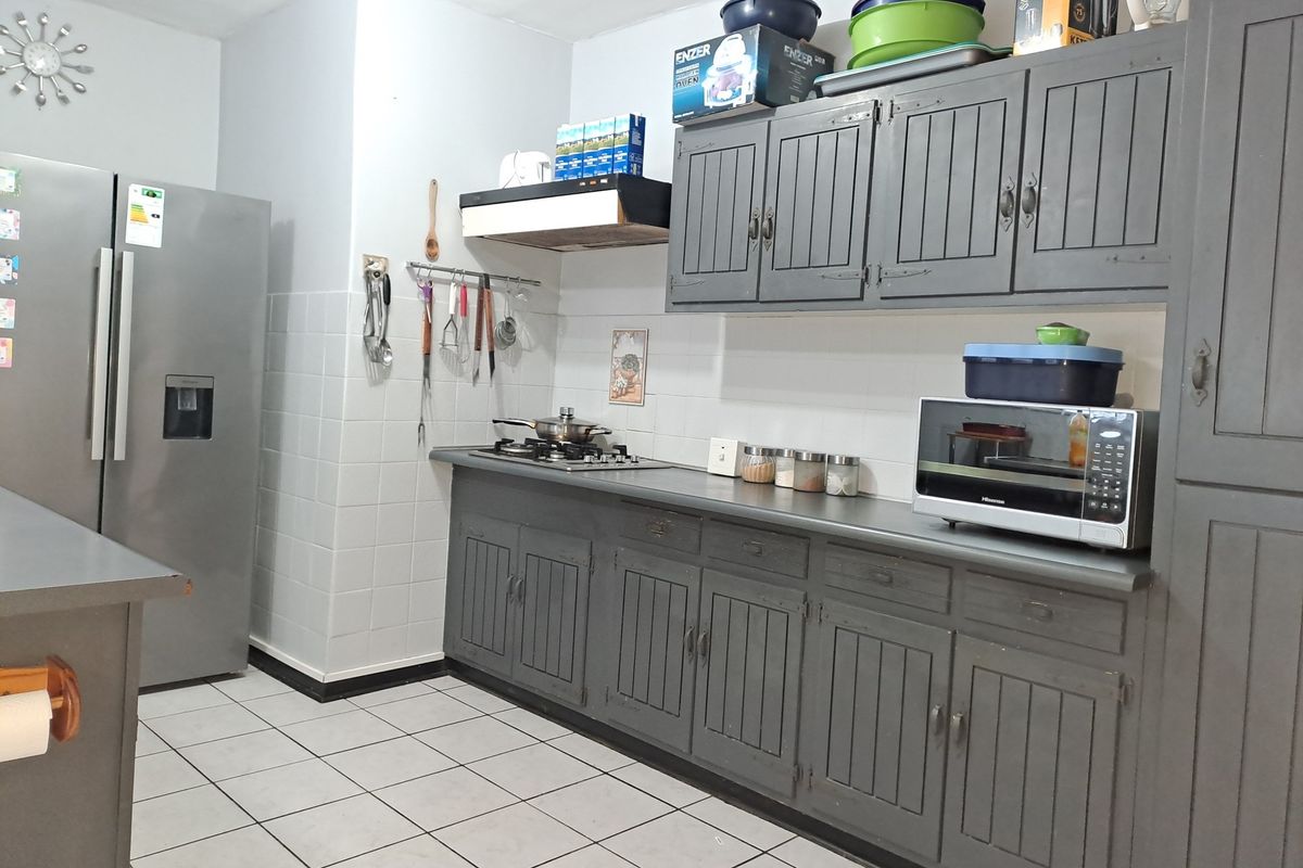 A functional kitchen featuring grey painted cabinetry, a gas hob with extractor fan, tiled splashbacks, and tiled flooring.