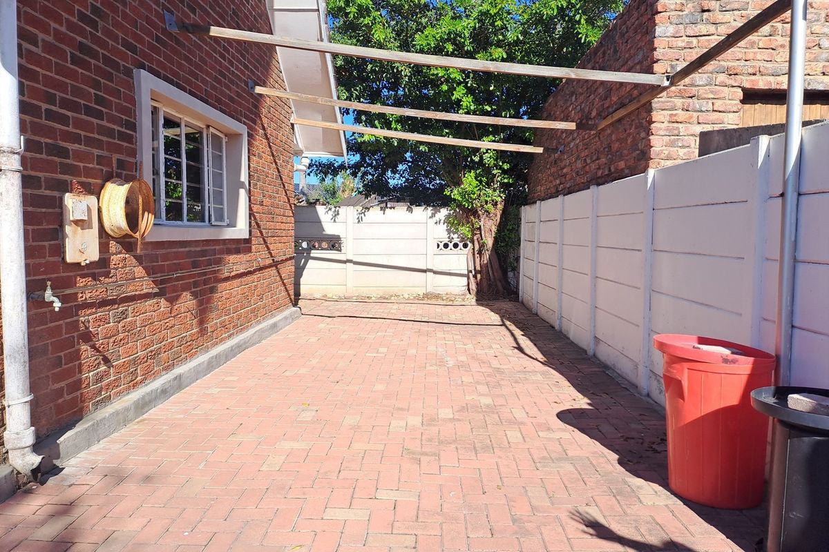 A paved rear courtyard area featuring a brick facade, precast boundary walls, and an open timber pergola structure.