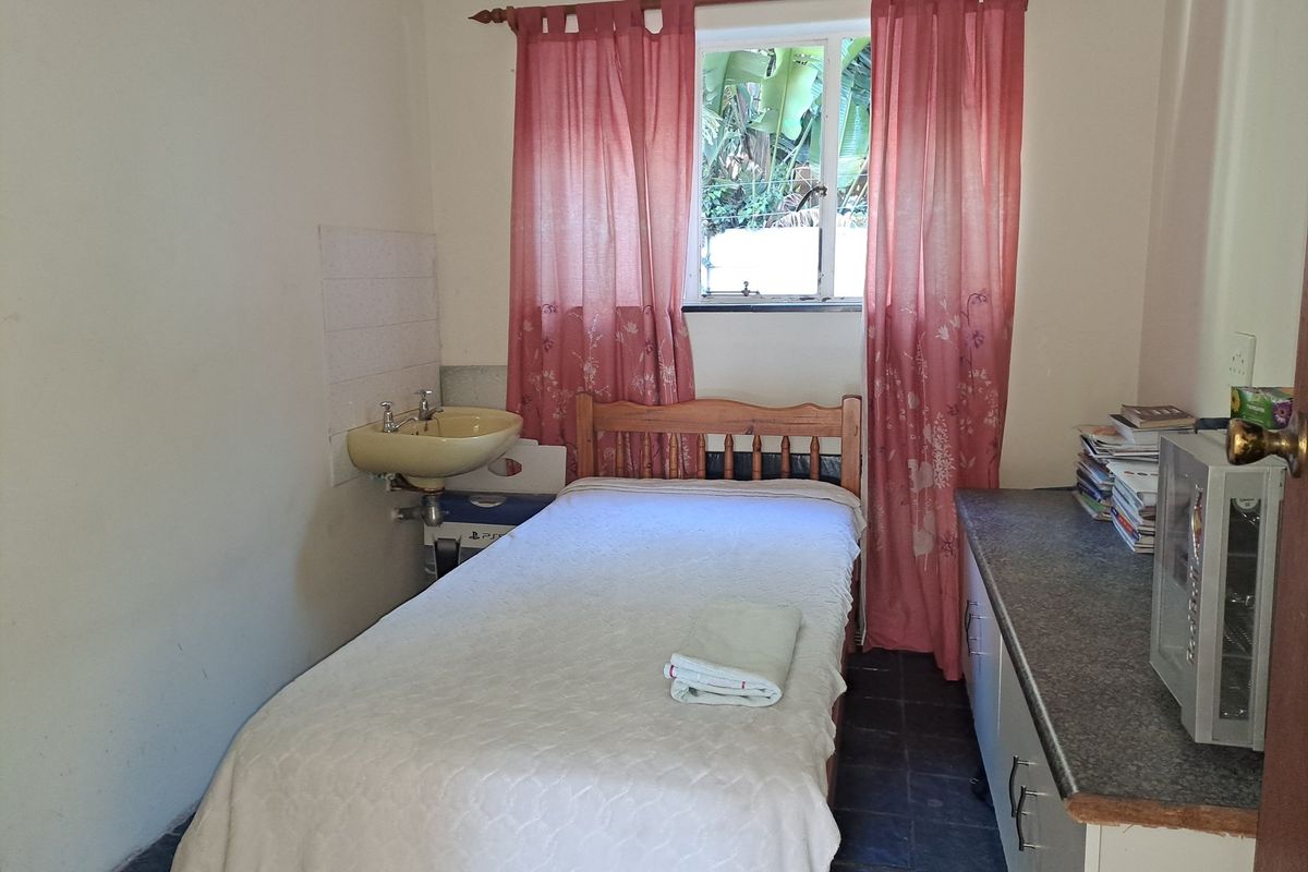 A compact bedroom featuring a wall-mounted basin, built-in cabinetry with a laminate countertop, and tiled flooring.