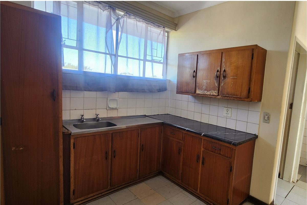 A dated kitchen featuring original wooden cabinetry, a stainless steel sink, and tiled splashbacks, offering a blank canvas for modern renovation.