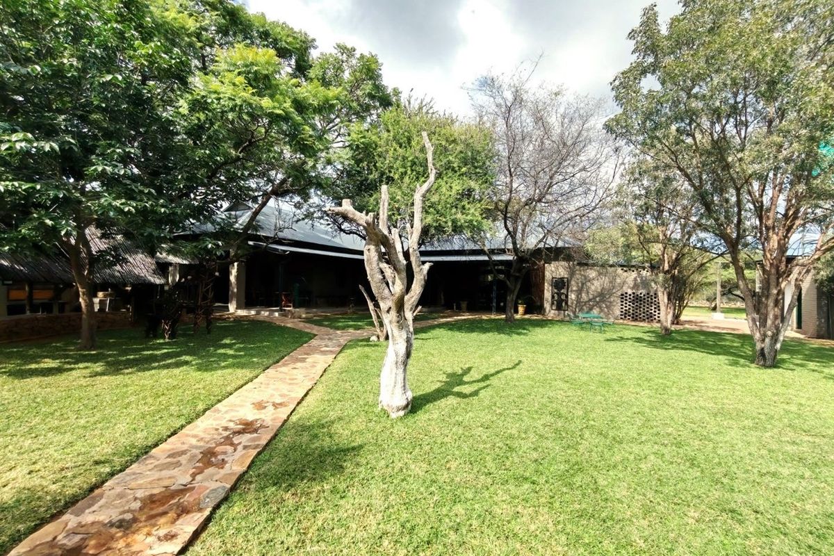A view of the farm property featuring a landscaped garden, stone pathway, and established trees leading to the main dwelling with a covered patio.