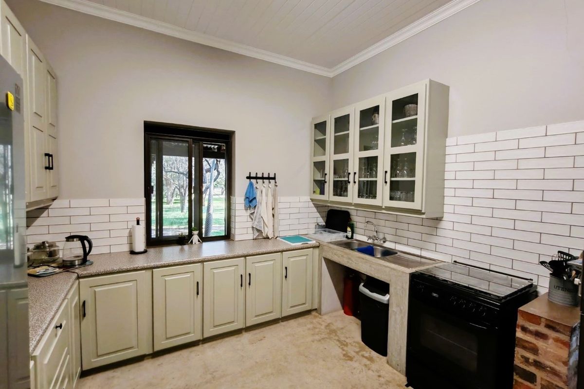 A functional kitchen featuring light-toned cabinetry, subway tile backsplash, granite-style countertops, and a built-in sink area with views of the farm grounds.