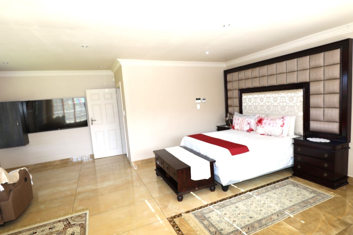 Spacious bedroom featuring large format tiled flooring, recessed downlighting, and a prominent custom built-in headboard with integrated bedside cabinetry.