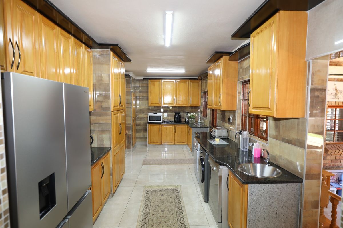 A functional kitchen featuring extensive wooden cabinetry, granite countertops, tiled backsplash, and tiled flooring with integrated appliance spaces.