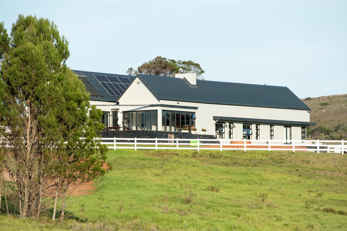 A view of the rear exterior of a modern residential property featuring a dark metal roof, solar panels, and a white picket fence.
