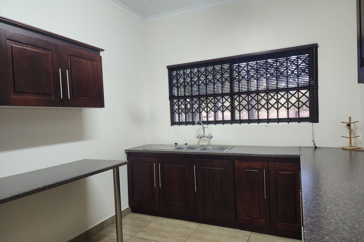 A functional kitchen area featuring dark wood cabinetry, granite-look countertops, a double stainless steel sink, and security bars on the window.