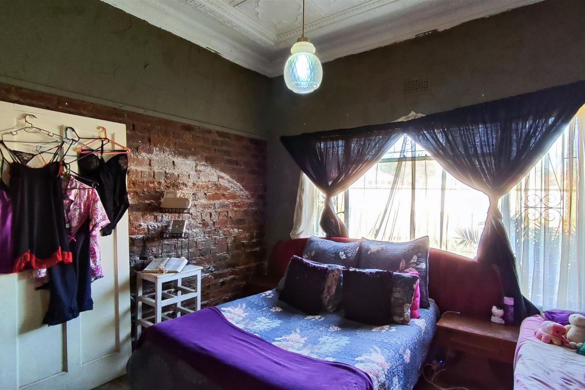 A bedroom featuring exposed brick walls, decorative ceiling molding, and a large window with security bars.