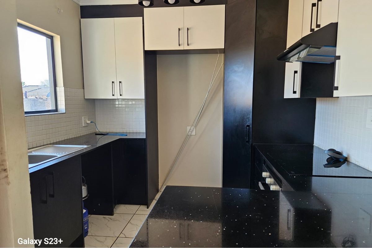 Modern kitchen featuring black and white cabinetry, granite countertops, tiled backsplash, and built-in oven with extractor fan.