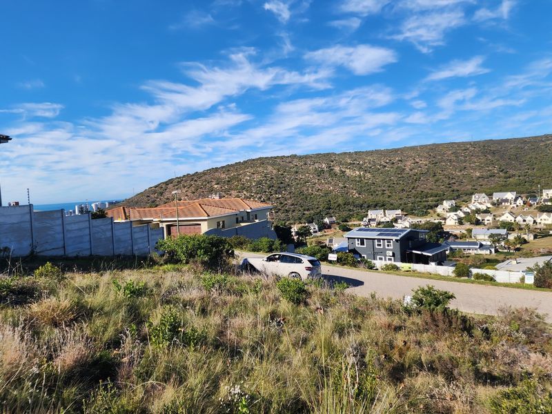 A view of a vacant residential plot in a hillside estate, featuring natural vegetation and surrounding suburban development.