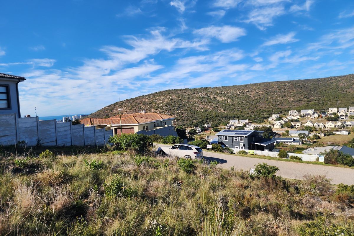 A view of a vacant residential plot in a hillside estate, featuring natural vegetation and surrounding suburban development.