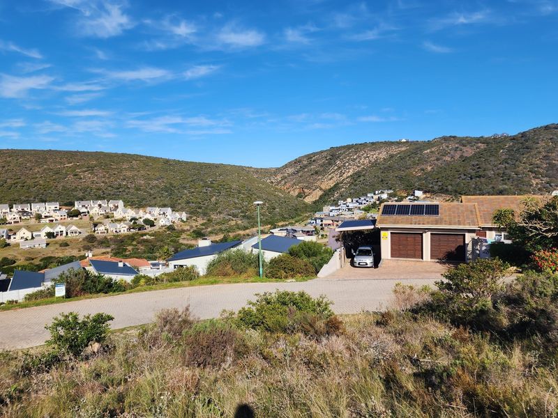 Elevated view of a residential neighborhood featuring a paved street, surrounding hills, and a nearby property with a double garage and solar panels.