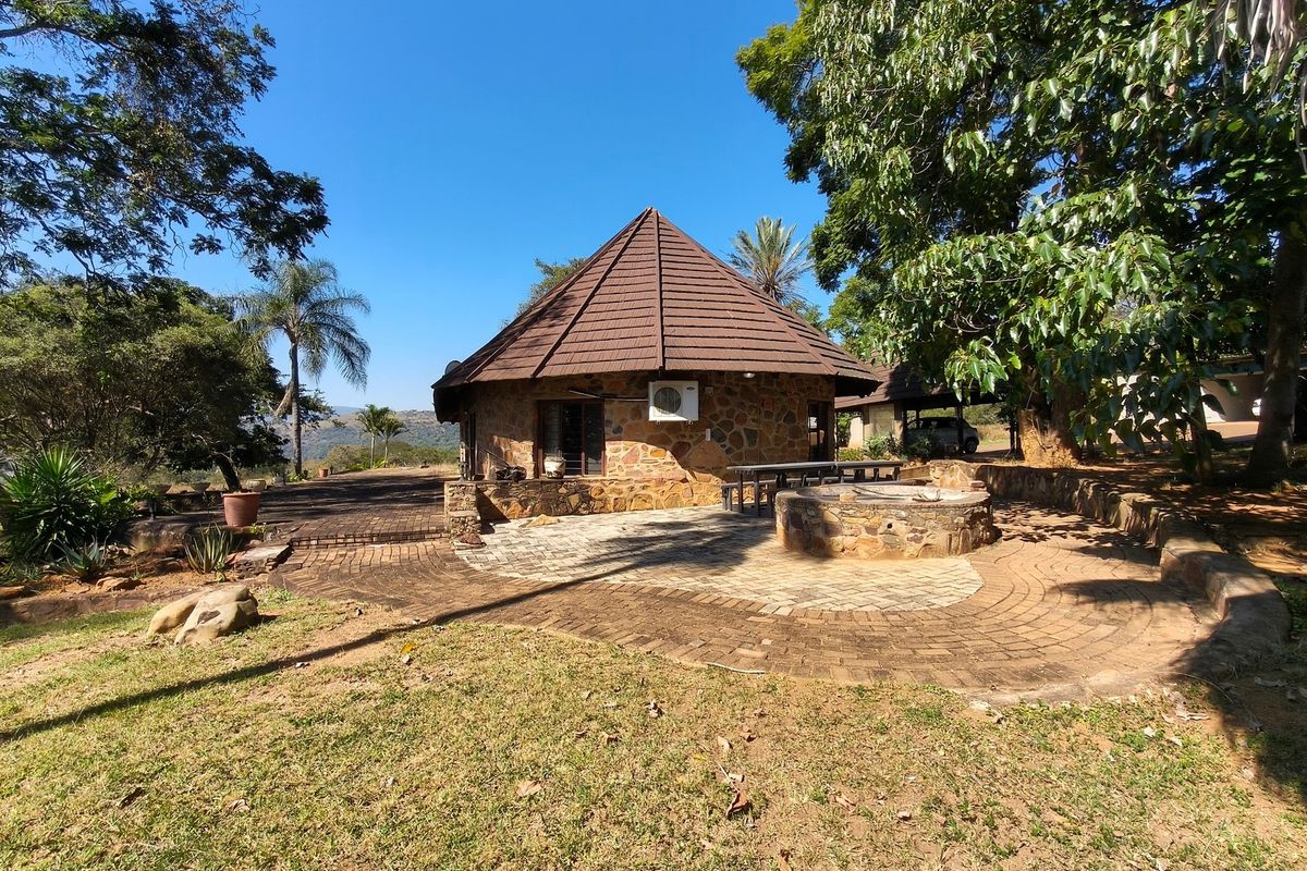 A rustic stone-clad dwelling with a pitched tiled roof, featuring a paved patio area and a circular stone fire pit in a garden setting.