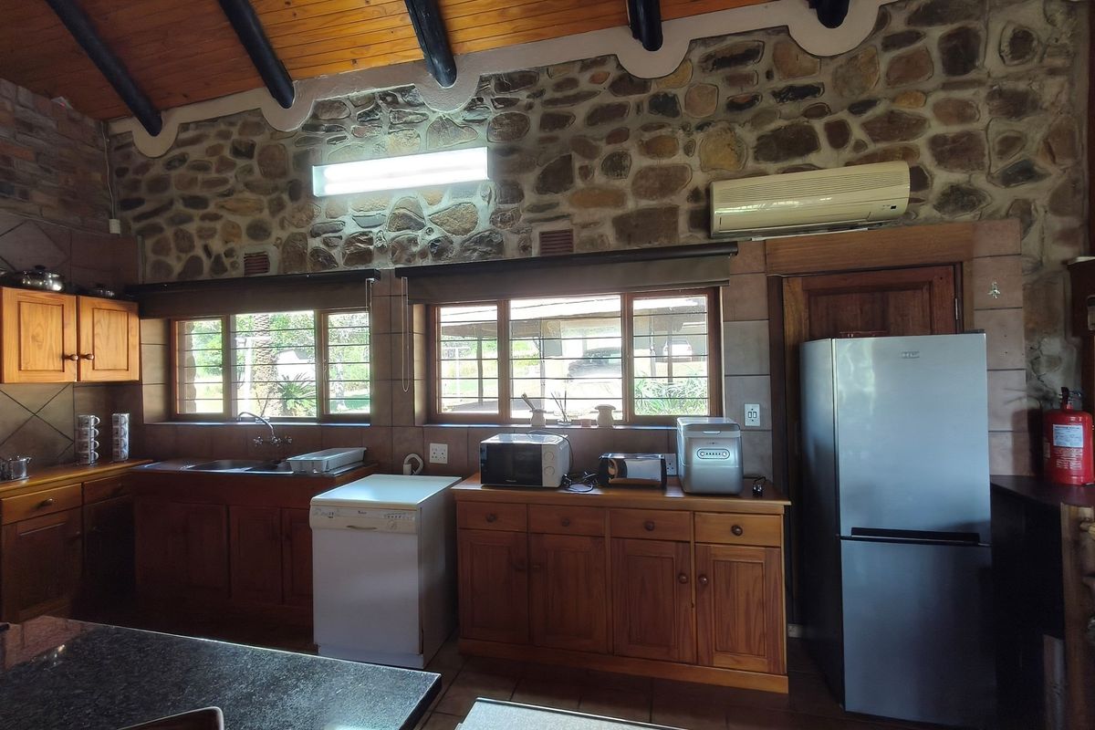 Rustic kitchen featuring exposed stone walls, timber ceiling beams, wooden cabinetry, and granite countertops with integrated sink and built-in storage.