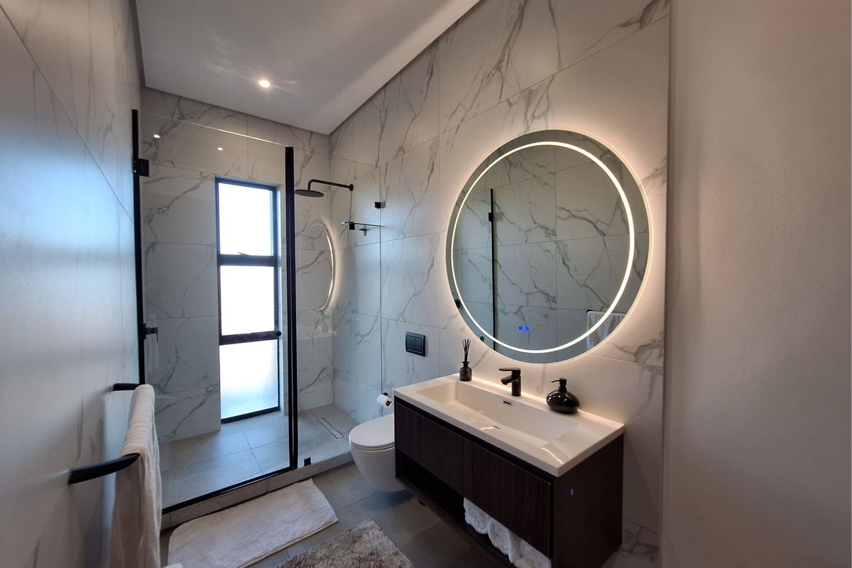 Modern bathroom featuring marble-look wall tiles, a floating vanity with integrated basin, a round LED-backlit mirror, and a walk-in shower with black frame.