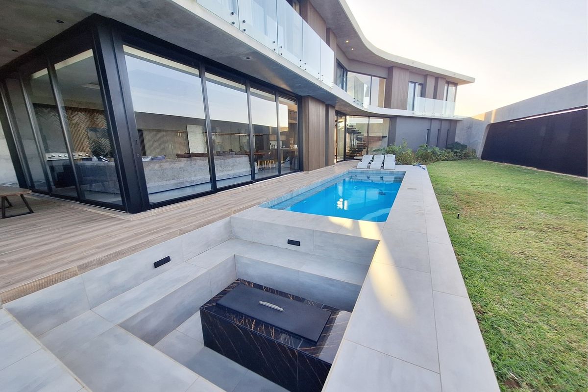Modern rear exterior featuring a swimming pool, sunken fire pit area, timber decking, and large glass sliding doors leading to the interior living space.