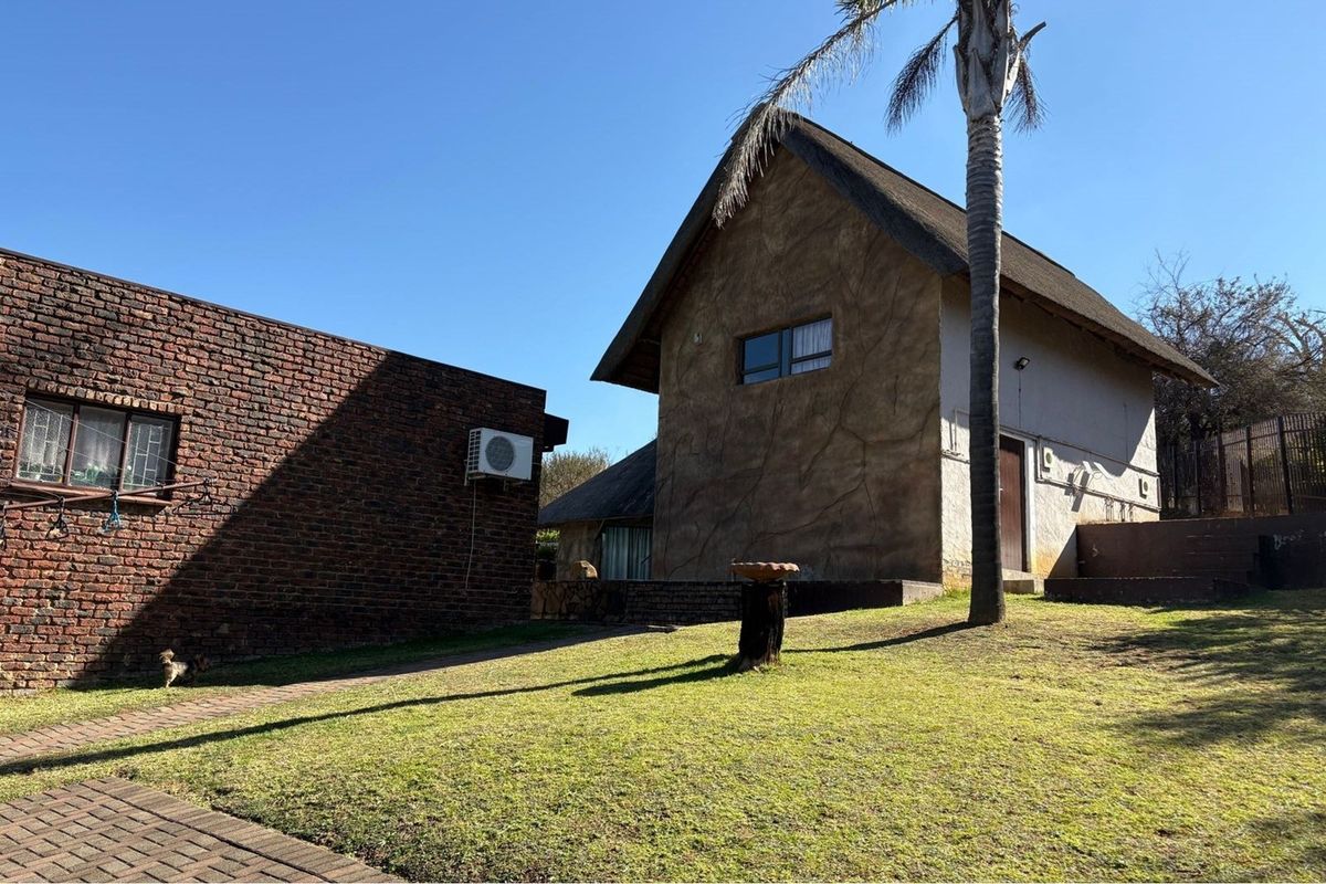 A view of the rear exterior of the property featuring a thatched roof structure, brick walling, and a landscaped garden area.