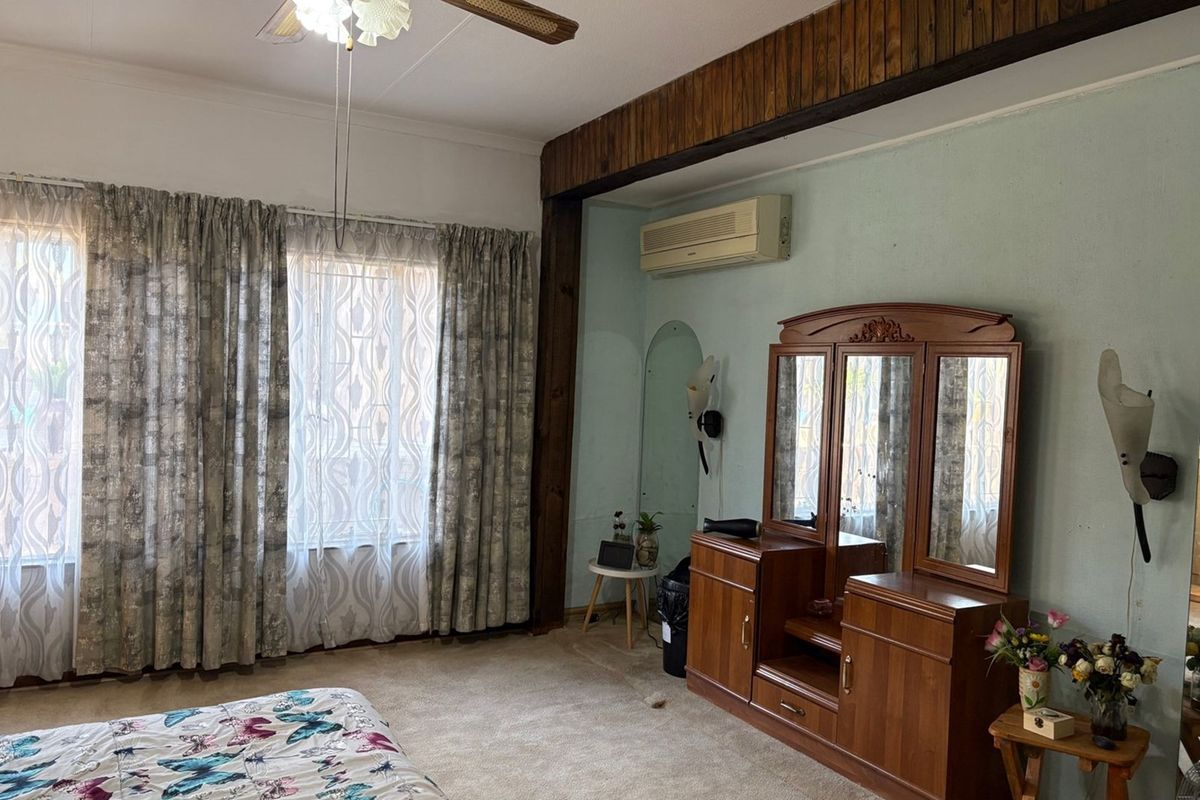 A spacious bedroom featuring a wall-mounted air conditioning unit, ceiling fan, and large windows with curtains.