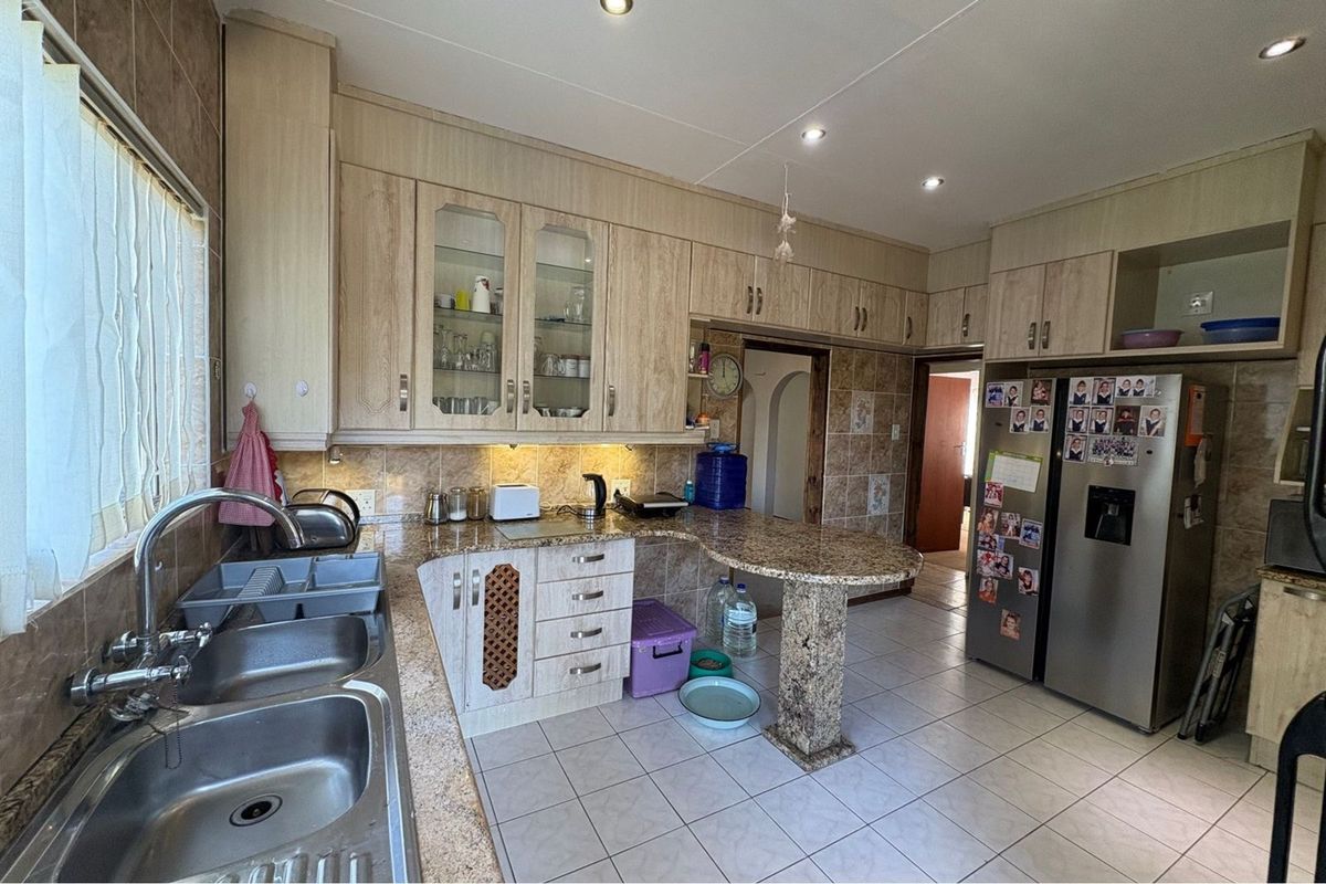A functional kitchen featuring light wood-grain cabinetry, granite countertops, a double stainless steel sink, and tiled flooring with integrated downlighting.