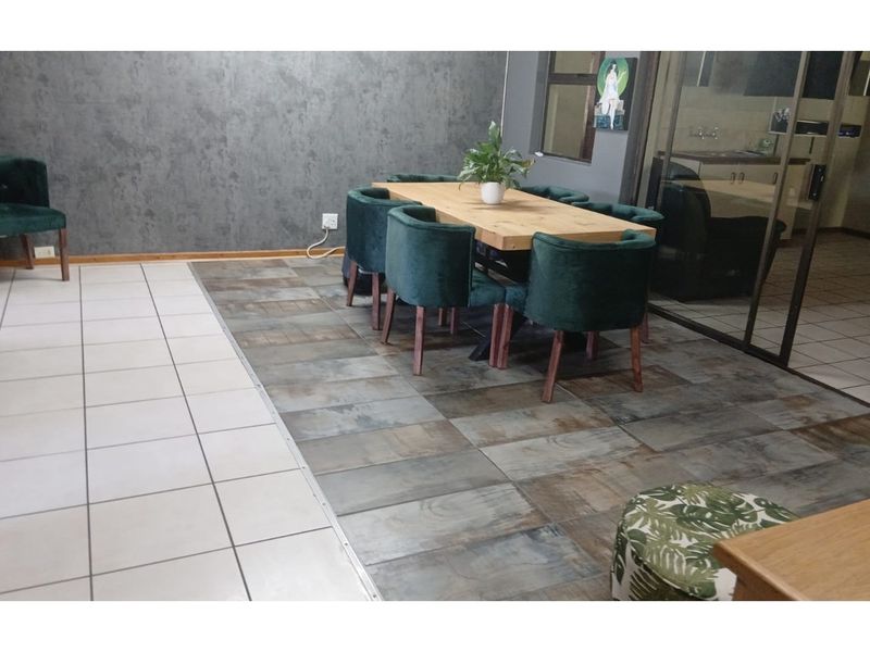 Open plan dining area featuring a mix of tiled flooring, textured feature wall, and glass partition leading to the kitchen area.