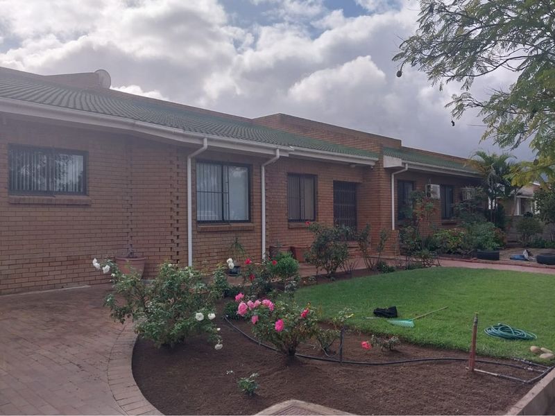 Front exterior view of a single-story brick house featuring a tiled roof, security bars on windows, and a landscaped front garden with paved driveway.