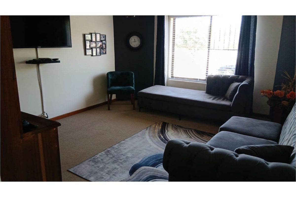 A comfortable living room featuring neutral walls, a dark accent wall, carpeted flooring, and a large window allowing natural light.
