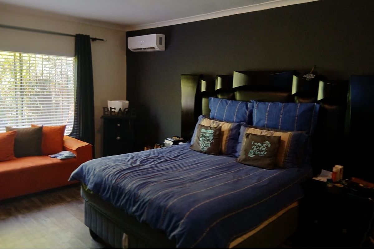 A bedroom featuring a wall-mounted air conditioning unit, dark accent wall, and large window with blinds.