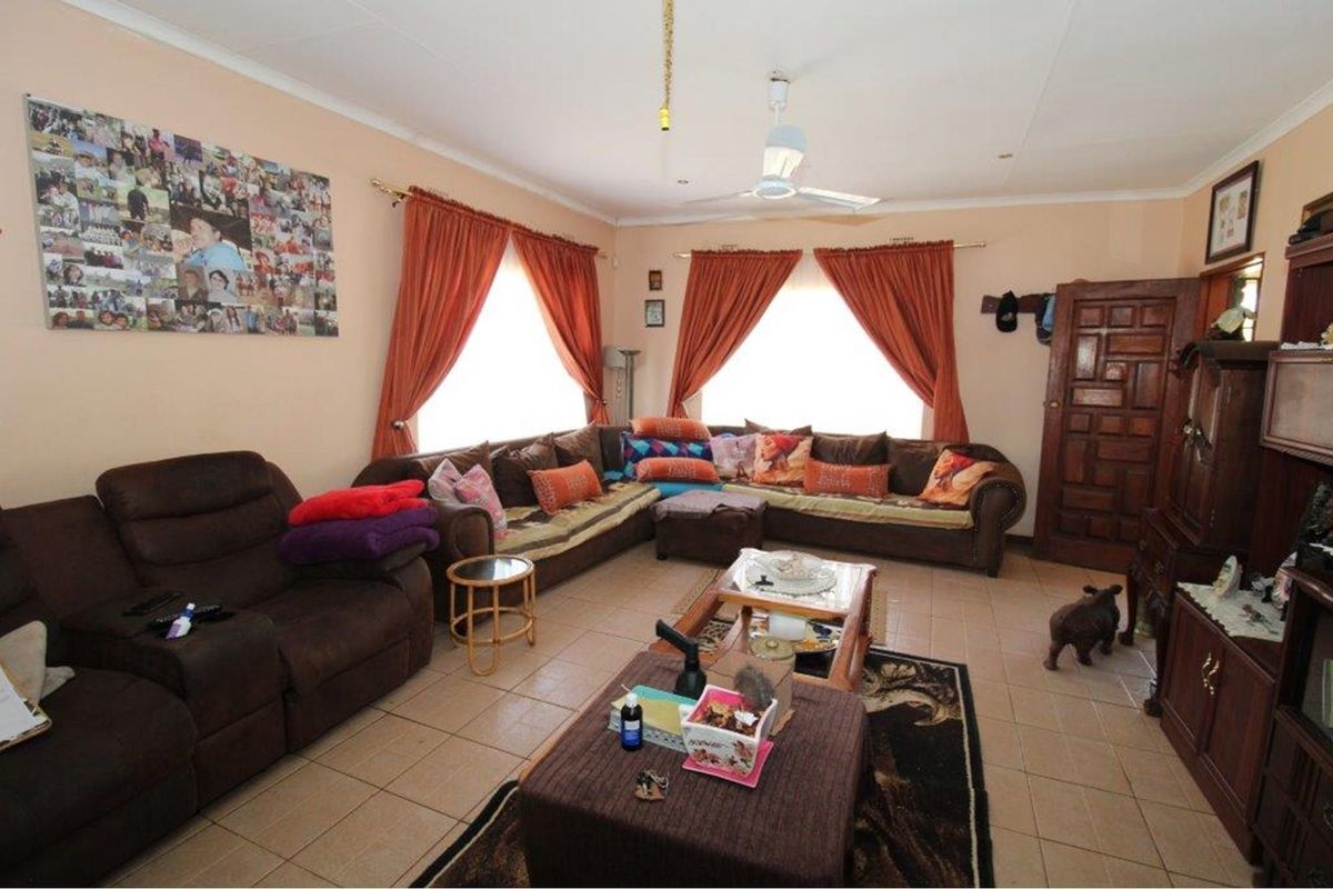 A spacious living room featuring tiled flooring, a ceiling fan, and large windows with curtain treatments.