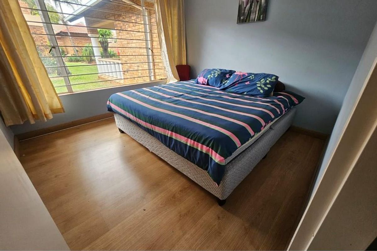 A bedroom featuring laminate flooring and a large window with security bars, offering a view of the exterior garden area.